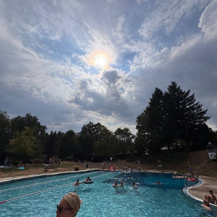 Ein großer Außenpool mit Schwimmern und Entspannung unter einem teilweise bewölkten Himmel.