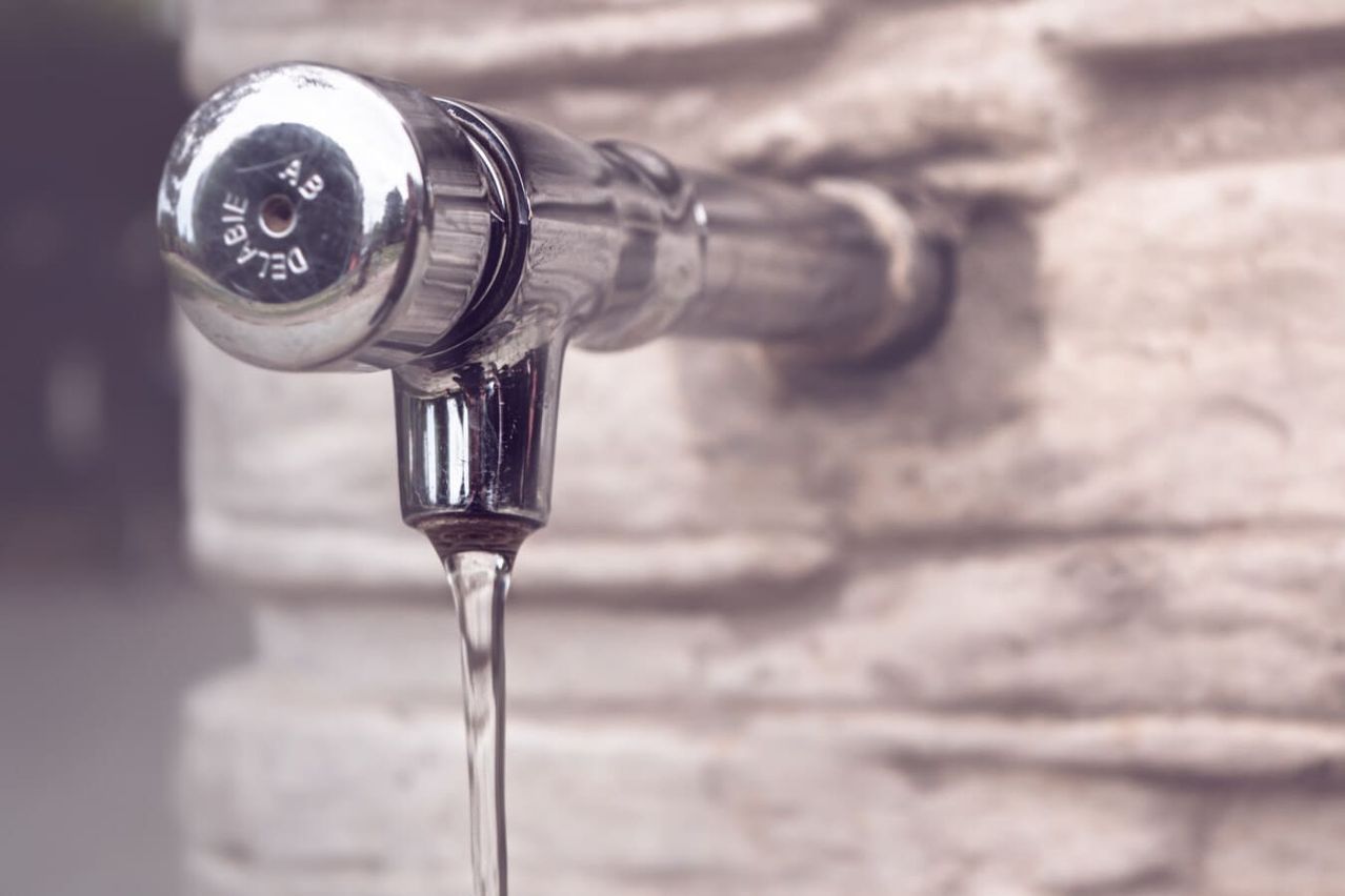 A close-up view of a stainless steel faucet with water dripping from it, mounted on a stone wall.
