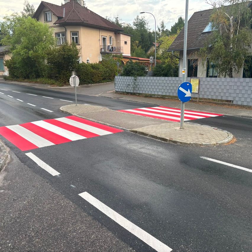 Zebrastreifen mit roter und weißer Markierung auf Asphaltstraße mit Wohnhaus im Hintergrund