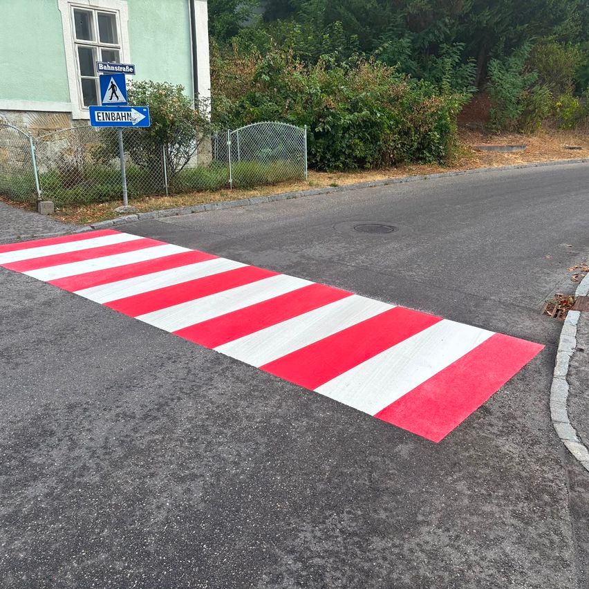 Eine rote und weiße gestreifte Fußgängerüberquerung ist auf einer Straße gemalt, mit einem Schild, das auf eine Fußgängerüberquerung hinweist.