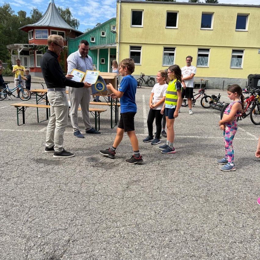 Zertifikatsübergabe an Kinder in einem Hof vor gelbem Gebäude
