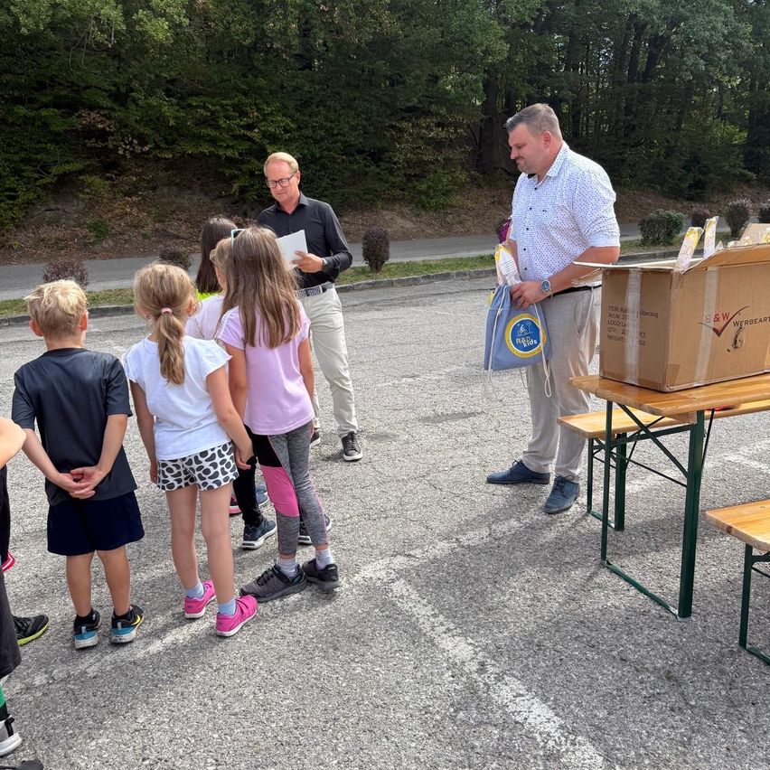 Kinder stehen vor Männern, die ihnen etwas erklären, ein Mann hält eine Tasche.