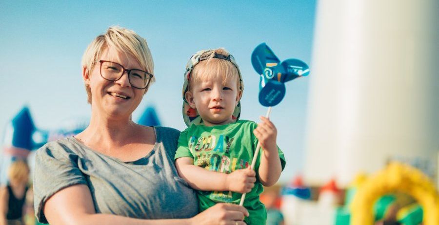 Eine Frau, die einen kleinen Jungen in einem Hut und einer Windmühle hält, mit einem verschwommenen Hintergrund von aufblasbaren Strukturen.