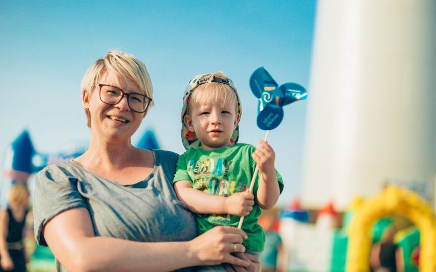 Eine Frau, die einen kleinen Jungen in einem Hut und einer Windmühle hält, mit einem verschwommenen Hintergrund von aufblasbaren Strukturen.