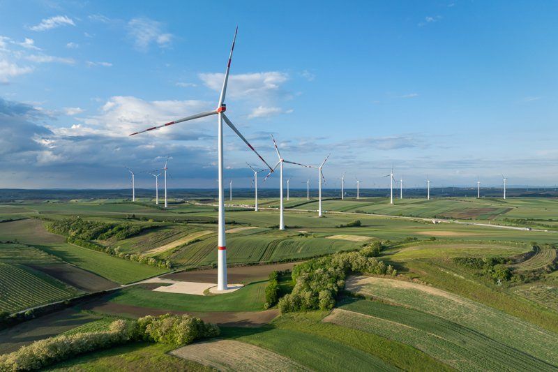 Luftaufnahme eines Windparks mit mehreren Windturbinen an einem sonnigen Tag, in einer grünen ländlichen Landschaft.