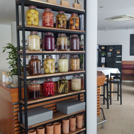 Ein hoher Metallregal gefüllt mit Gläsern, die Früchte und Gemüse eingelegt enthalten, in einer Küche.