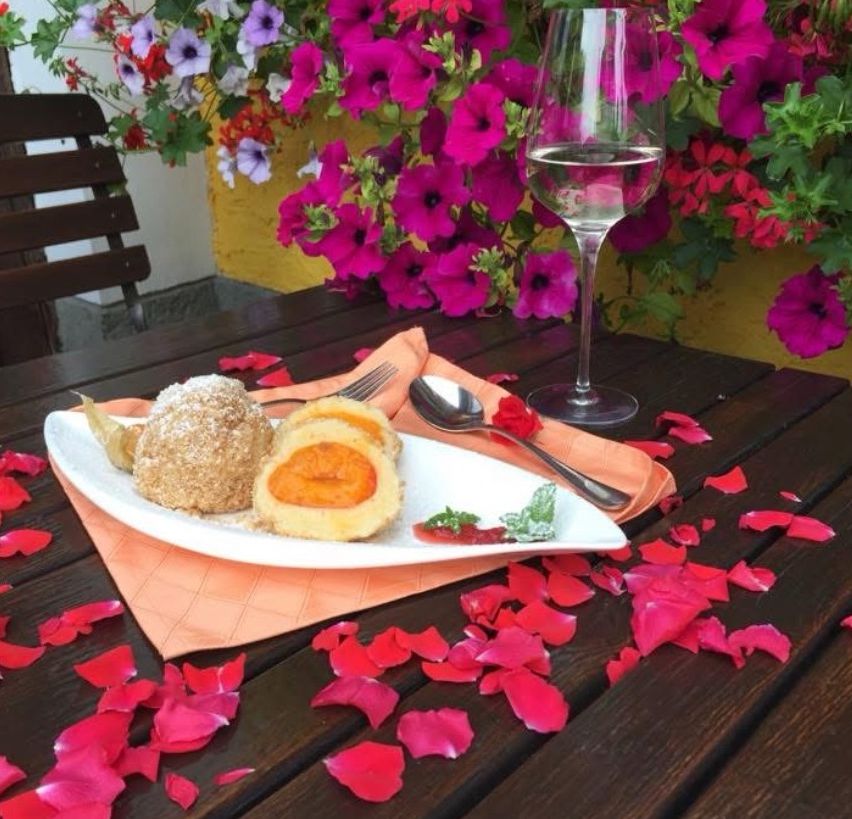 Ein Teller mit Dessert, Löffel, Gabel und Weinglas auf einem Holztisch. Im Hintergrund ist eine Blumendekoration.