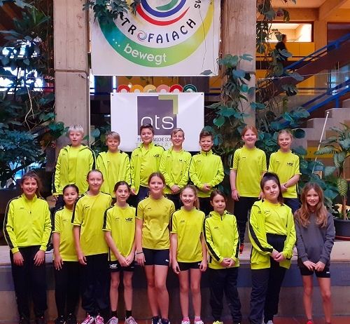 Eine Gruppe von Kindern in gelber Sportbekleidung posiert für ein Foto vor einem Gebäude mit einem Banner.