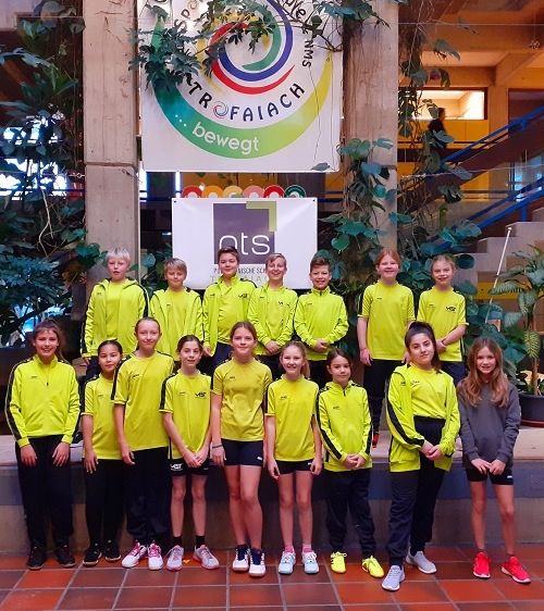 Eine Gruppe von Kindern in gelber Sportbekleidung posiert für ein Foto vor einem Gebäude mit einem Banner.