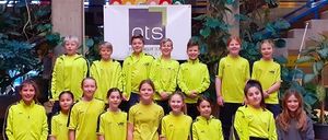 Eine Gruppe von Kindern in gelber Sportbekleidung posiert für ein Foto vor einem Gebäude mit einem Banner.