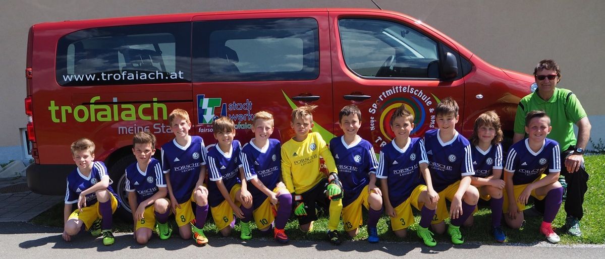 Eine Gruppe junger Fußballspieler in blauen und gelben Trikots posiert für ein Foto vor einem roten Van mit der Aufschrift "Stadtwerkstatt".