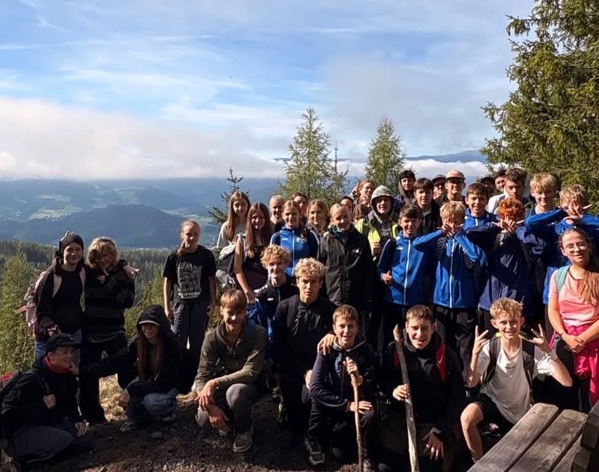 Eine Gruppe junger Menschen posiert für ein Foto auf einem Berg mit einer malerischen Kulisse.