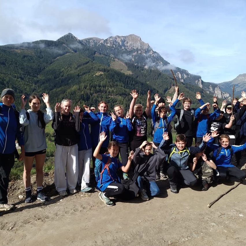 Eine Gruppe von Menschen in blauen Jacken posiert für ein Foto auf einem Bergpfad mit einer malerischen Kulisse.
