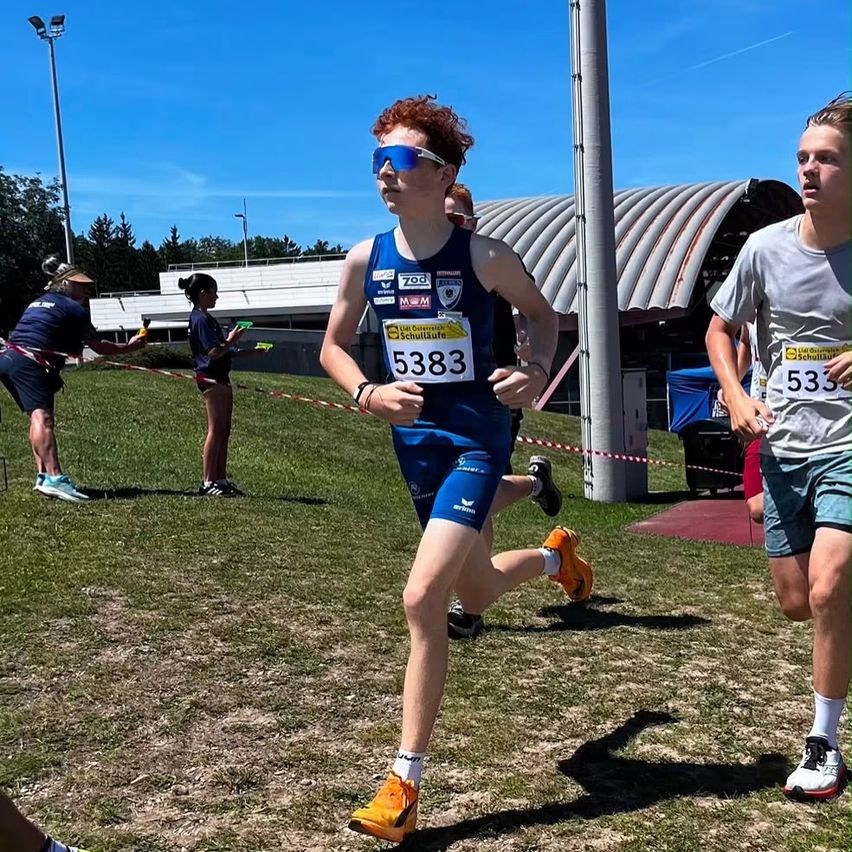 Ein Läufer mit blauen und orangefarbenen Turnschuhen nimmt an einem Marathon teil. Ein anderer Läufer folgt ihm dicht auf den Fersen. Zuschauer stehen in der Nähe.