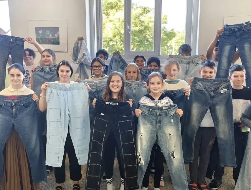 Eine Gruppe von Kindern und Jugendlichen hält ihre Jeans hoch, lächelt und posiert für ein Foto.