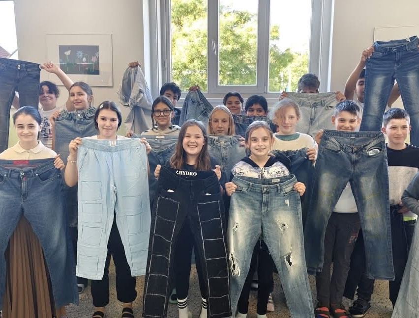 Eine Gruppe von Kindern und Jugendlichen hält ihre Jeans hoch, lächelt und posiert für ein Foto.
