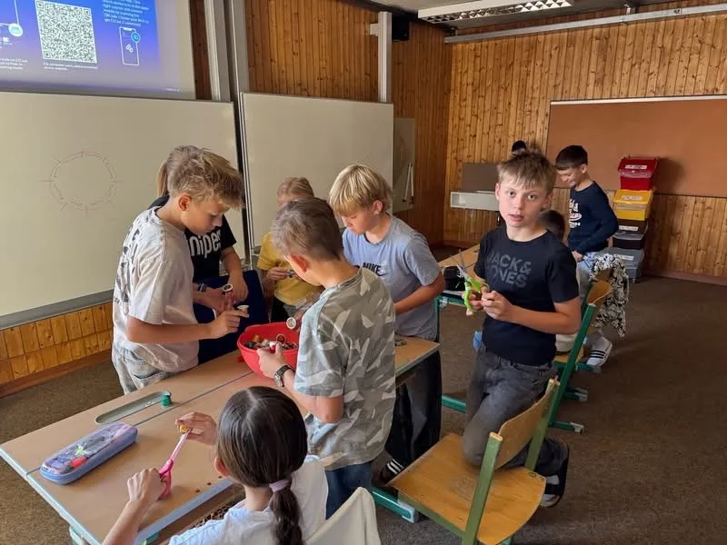 Eine Gruppe von Kindern ist in einem Klassenzimmer und macht eine Aktivität mit kleinen Objekten.