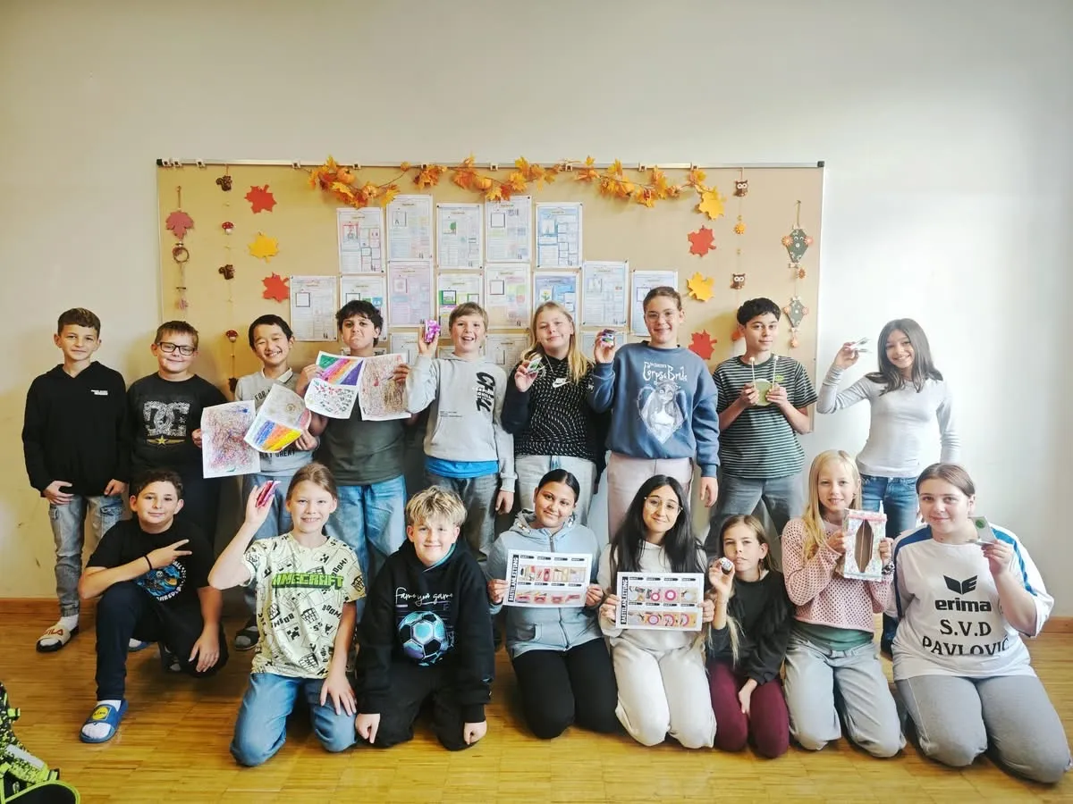 Eine Gruppe von Kindern posiert für ein Foto im Klassenzimmer. Sie halten Papierstücke mit Zeichnungen und Text hoch.