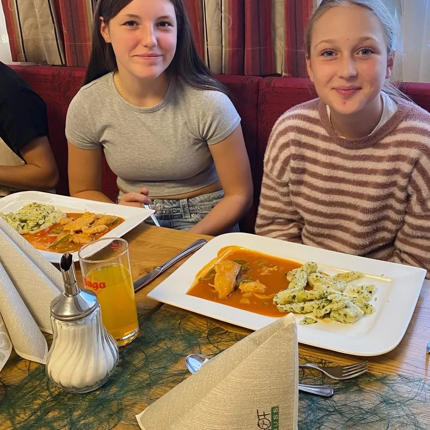 Zwei junge Mädchen sitzen an einem Tisch in einem Restaurant und lächeln für ein Foto.