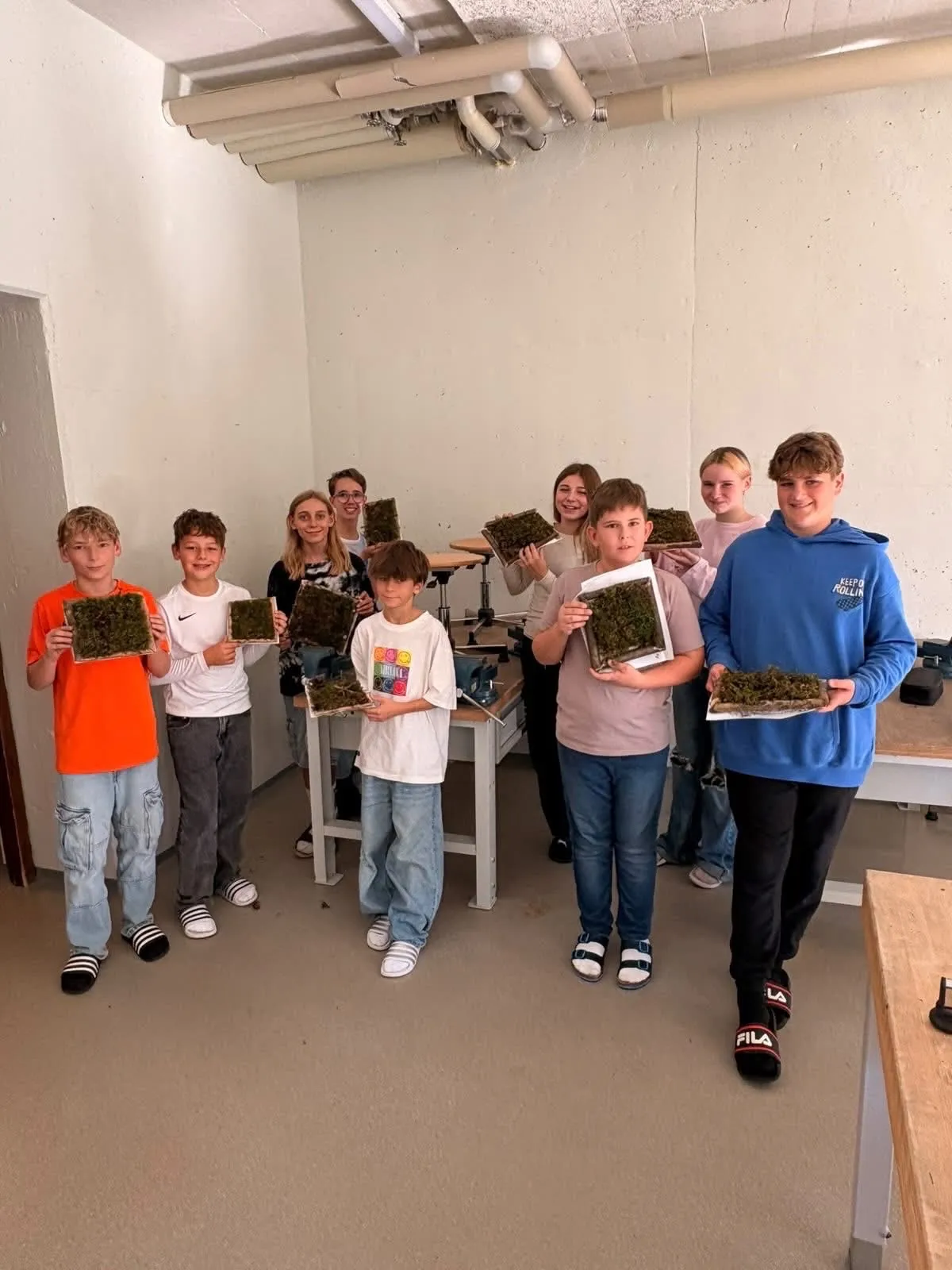 Eine Gruppe von Kindern in einem Raum, jeder hält ein Stück grünen Moos auf einem Brett.