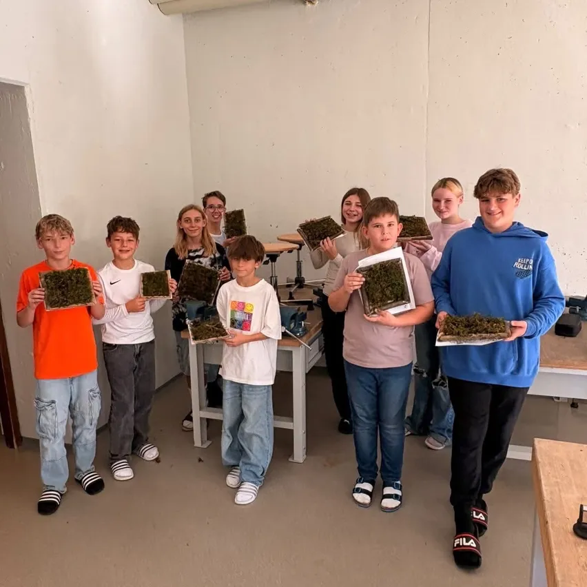 Eine Gruppe von Kindern in einem Raum, jeder hält ein Stück grünen Moos auf einem Brett.