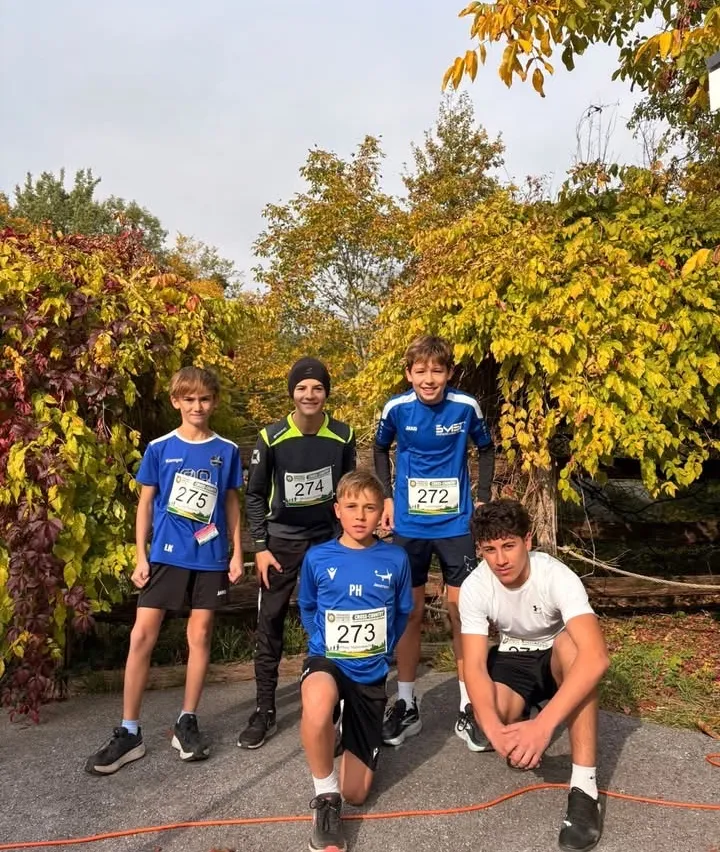 Fünf Jungen stehen in einer Reihe und tragen Sporttrikots mit Nummern. Sie posieren für ein Foto vor Bäumen mit gelben Blättern.