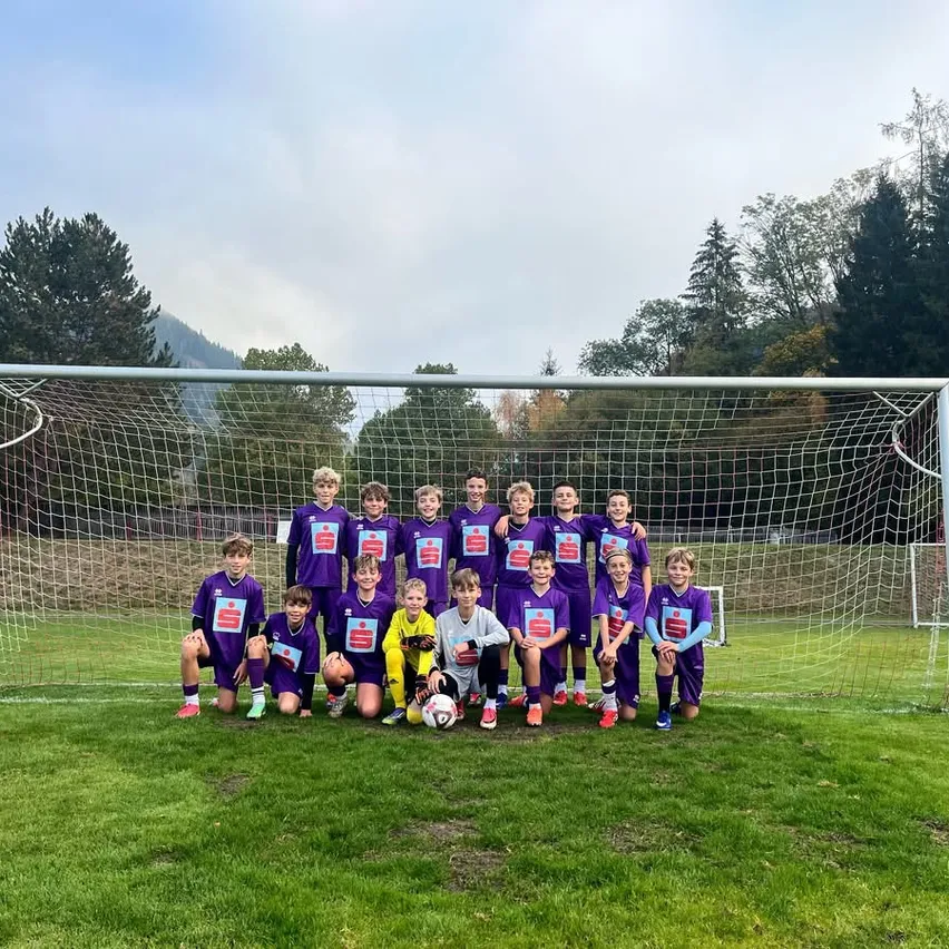 Eine Gruppe junger Fußballspieler in lila Trikots posiert für ein Foto vor einem Tor auf einem Rasenfeld.