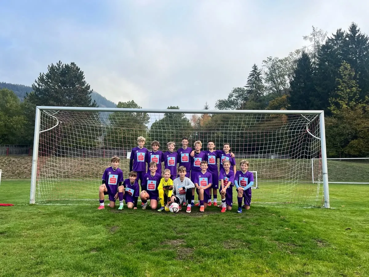 Eine Gruppe junger Fußballspieler in lila Trikots posiert für ein Foto vor einem Tor auf einem Rasenfeld.