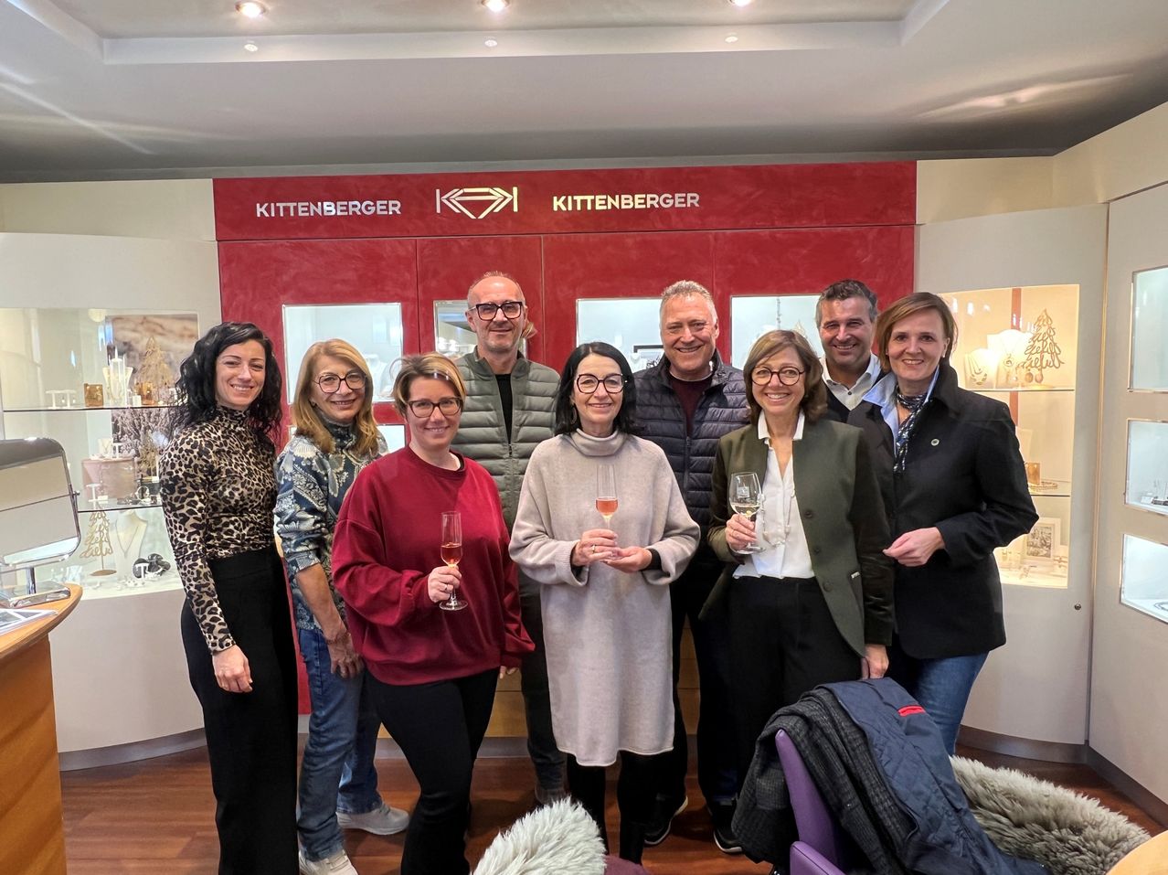 Eine Gruppe von Menschen, die vor einer roten Wand mit dem Wort Kittenberger darauf stehen. Sie halten alle Weingläser.