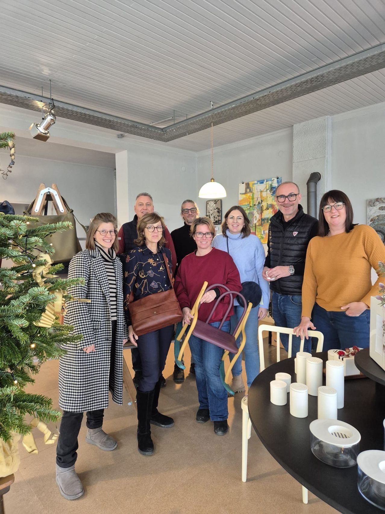 Eine Gruppe von Menschen posiert für ein Foto in einem Raum mit einem Weihnachtsbaum, Handtaschen und Kunstwerken an den Wänden. Ein Tisch mit Kerzen und Stühlen ist ebenfalls zu sehen.
