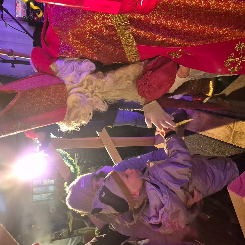 Eine Figur von Santa Claus mit einem roten Kostüm und weißem Bart interagiert mit zwei Kindern in einem schwach beleuchteten Raum.