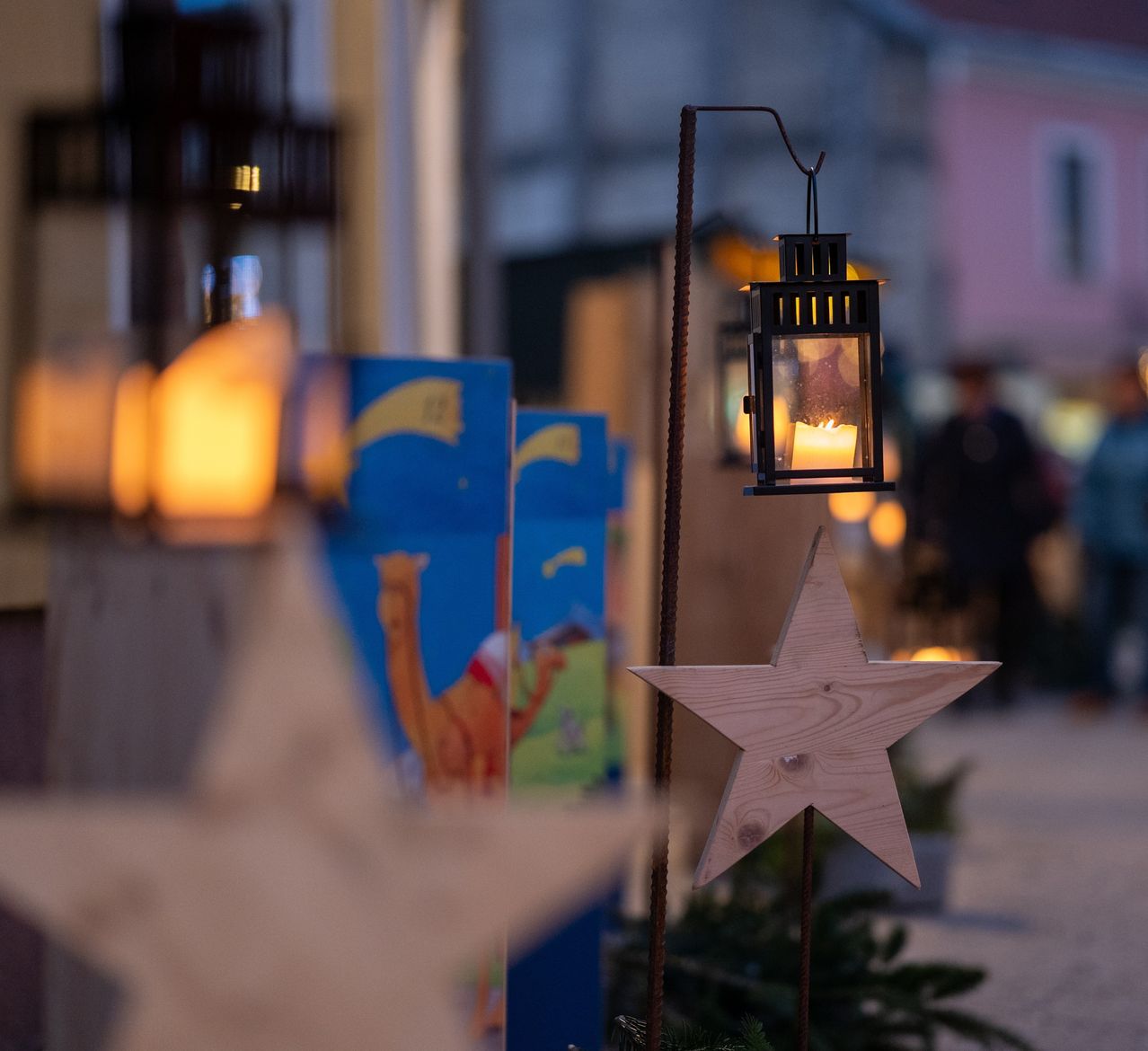Beleuchtete Laternen und Sternendekorationen sind im Freien bei Dämmerung ausgestellt. Ein Kamel ist auf einem blauen Plakat abgebildet.