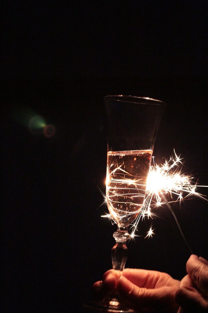 Ein Champagnerglas mit Champagner wird in einer dunklen Umgebung von einem Feuerwerkskörper beleuchtet.