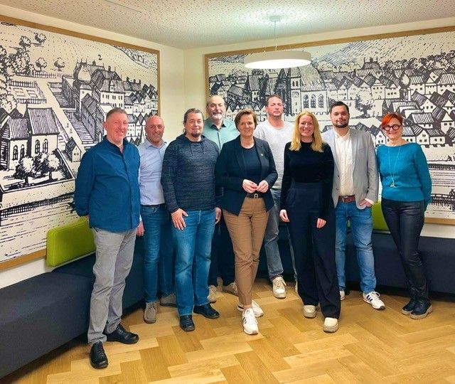 Eine Gruppe von Menschen steht in einem Büro mit Holzböden und Stadtgemälden an den Wänden und lächelt für ein Foto.