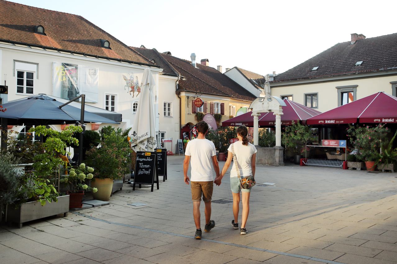 Ein Paar geht Hand in Hand über einen Außenplatz mit Geschäften und Restaurants.