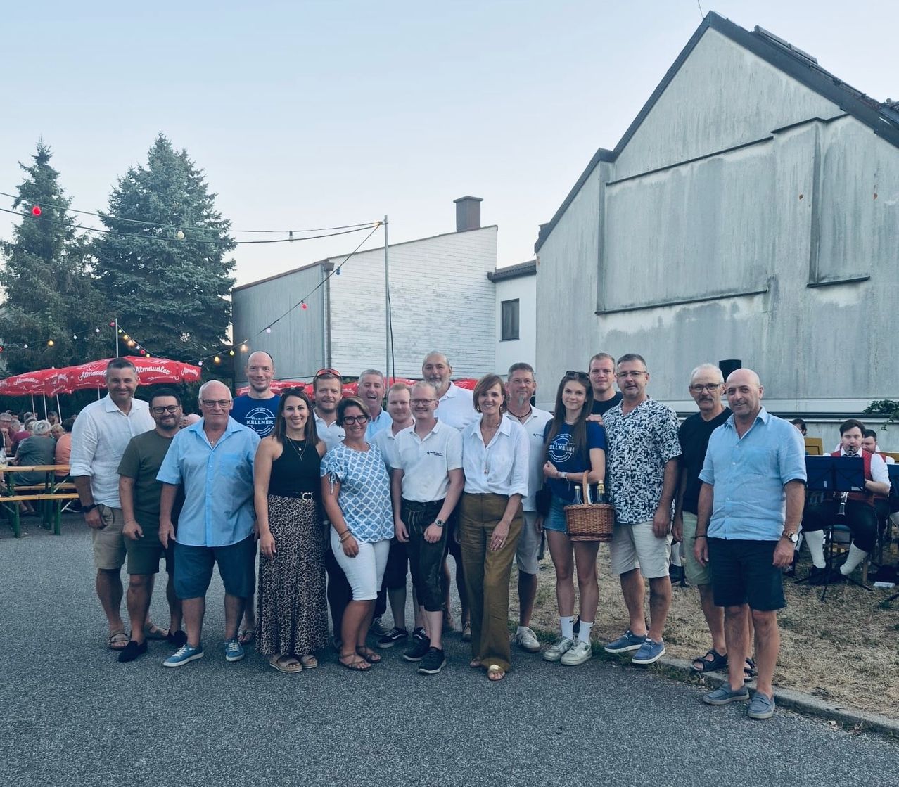 Eine Gruppe von Menschen, sowohl Männer als auch Frauen, stehen zusammen vor einem Gebäude und lächeln für ein Foto.