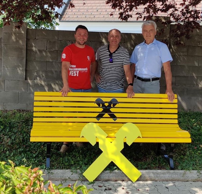  GR Michael Kramer, Obmann des DEV Helmut Kaufmann und Herr Reinhard Riedl (Bankstellenleiter Schrattenberg) stehen vor einer gelben Bank, die von der Raika gesponsert wurde