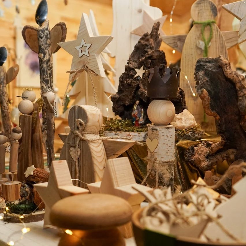 Eine Sammlung von Holzweihnachtsschmuck, darunter Sterne, Bäume und Figuren, auf einem Tisch mit Lichtern und einem Holzstumpf angeordnet.