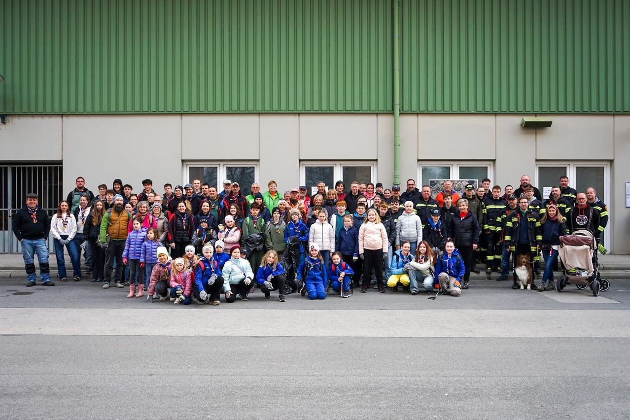 A group of individuals stands in front of a building, including firefighters, children, and adults, some in winter attire, posing for a photo.