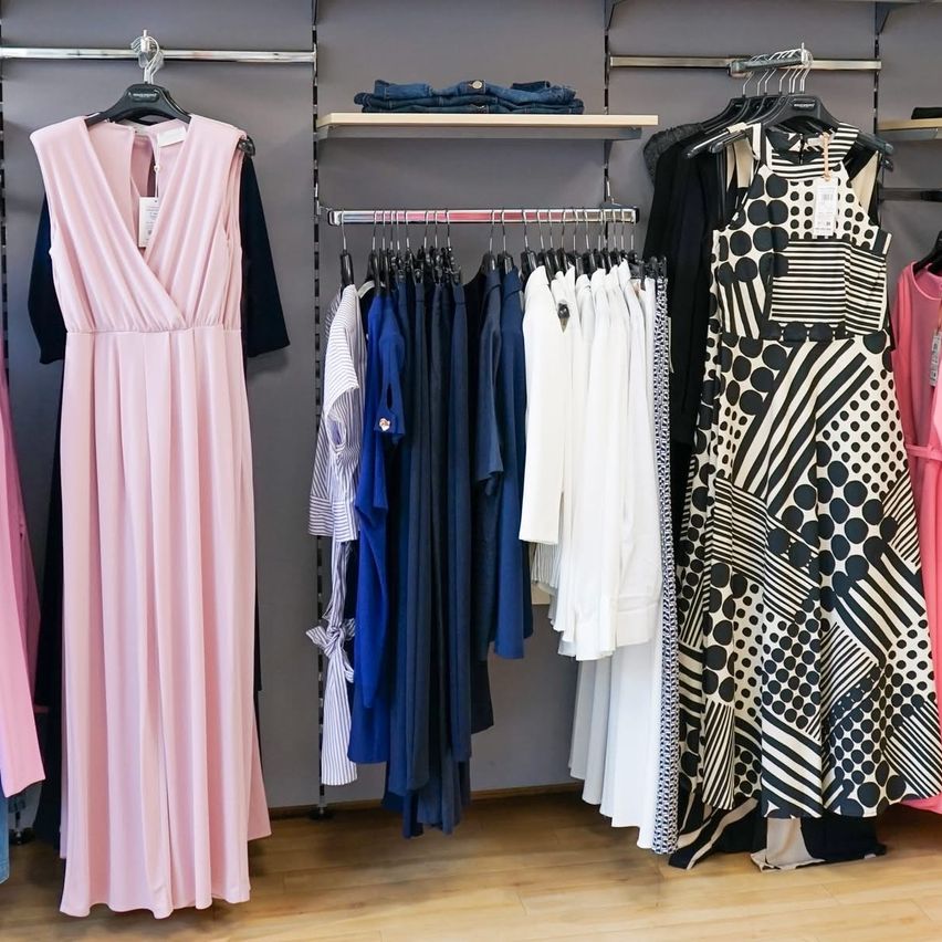A clothing store displays a variety of dresses. A pink dress is on the left, and a black and white polka-dot dress is on the right. The middle section features a row of dresses in blue, white, and other colors.