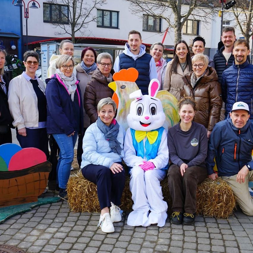 A group of people, including a person in a bunny costume, are posing for a picture on a cobblestone street.