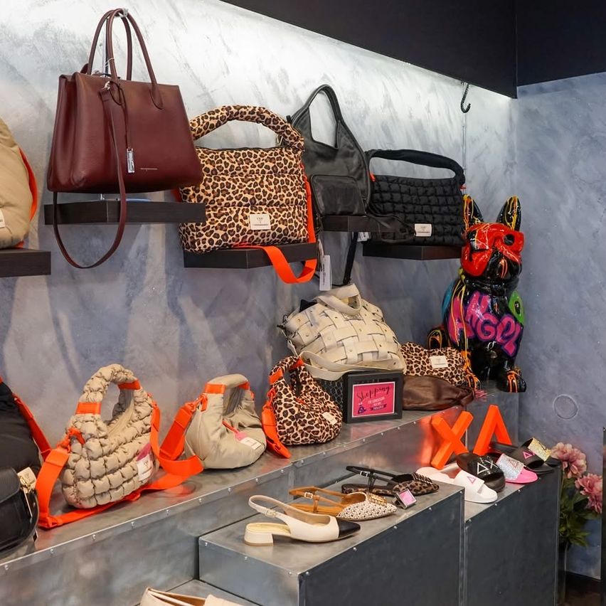 A store displays handbags and shoes on shelves. Various bags and shoes are organized with some on the wall and others on metal shelves.