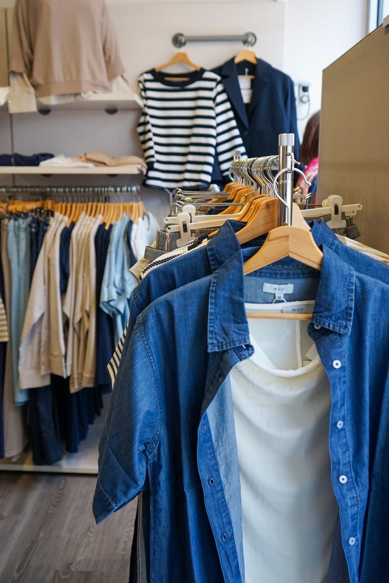 A clothing rack with various blue and white shirts, some folded and others hanging. The denim shirt is prominently displayed.