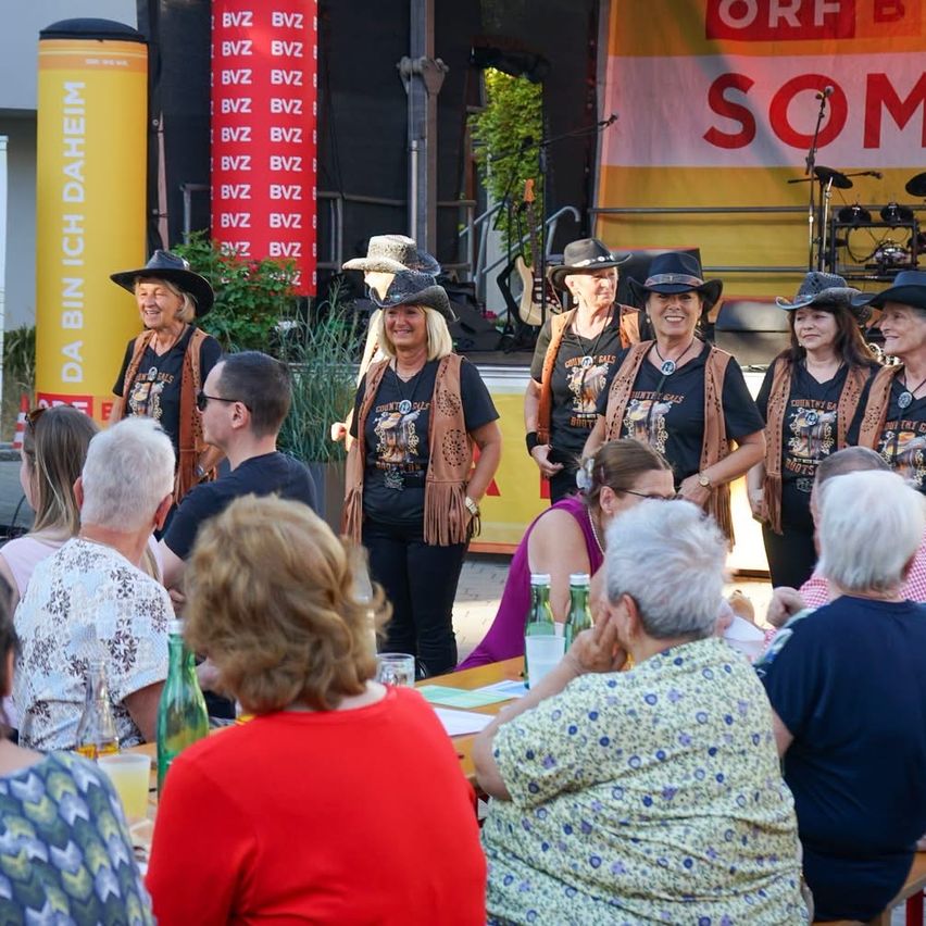 Eine Gruppe von Frauen in Cowboy-Hüten tritt auf einer Bühne vor einem Publikum auf.