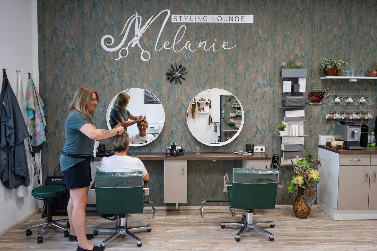 Eine Frau lässt sich in einem Salon die Haare stylen, mit einem großen Spiegel und einer Uhr an der Wand.