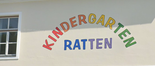 Ein weißes Gebäude mit einem farbenfrohen 'KINDERGARTEN RATTEN'-Schild an der Wand und einem Fenster in der Ecke.