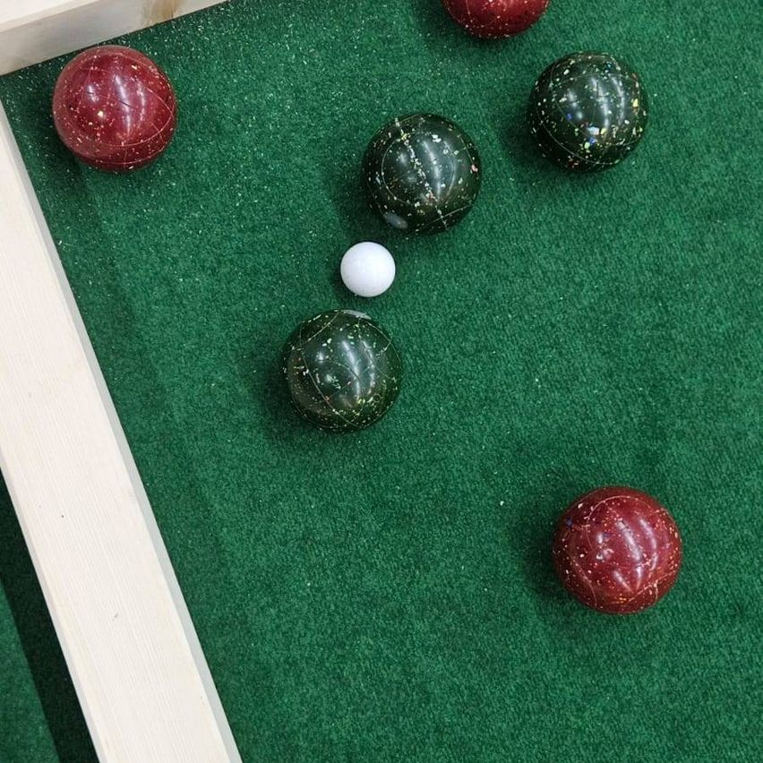 Eine Nahaufnahme eines Billardtisches mit mehreren Kugeln, darunter ein weißer Ball und fünf rote und grüne Bälle. Die Kugeln liegen auf einer grünen Filzoberfläche.