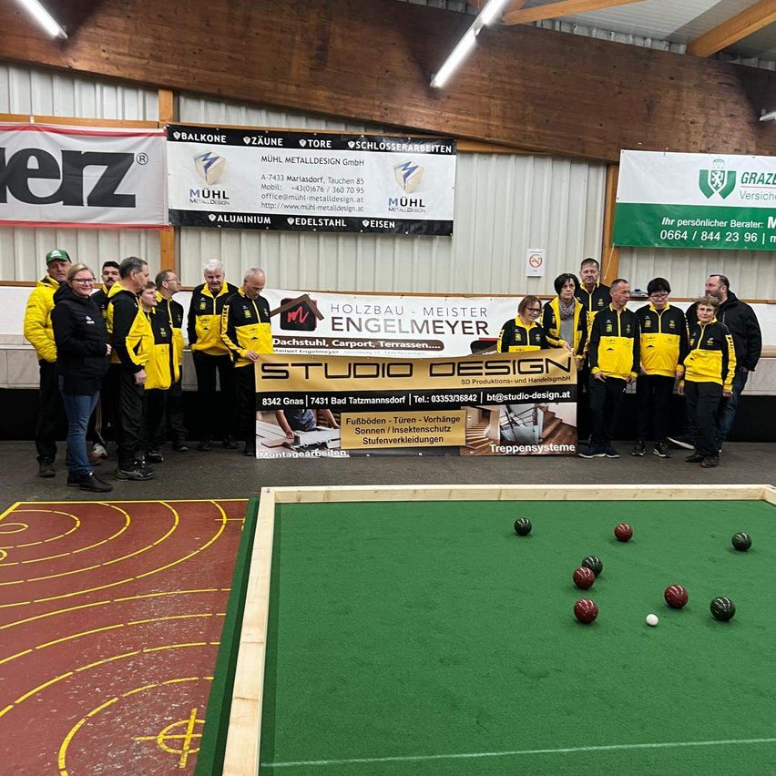 Eine Gruppe von Menschen in gelben und schwarzen Jacken steht hinter einem Banner in einem Raum mit einem Billardtisch. Werbung und Schilder sind an den Wänden angebracht.