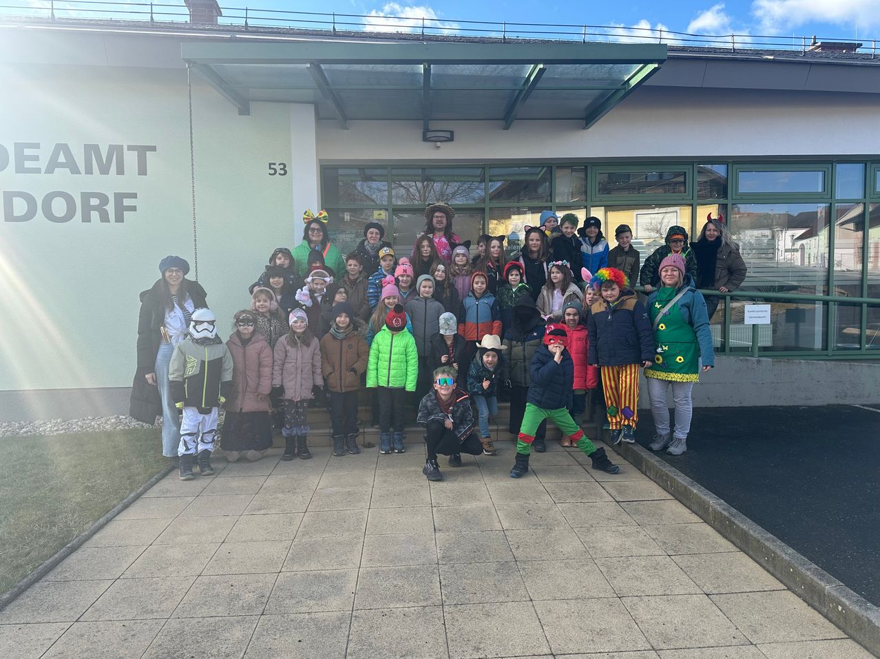 A group of children and adults dressed in various costumes pose for a photo in front of a building.