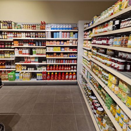 Ein Innenraum eines gut sortierten Lebensmittelgeschäfts mit Regalen voller verschiedener Produkte, darunter Saucen, Gewürze und Konserven, unter warmer Beleuchtung.
